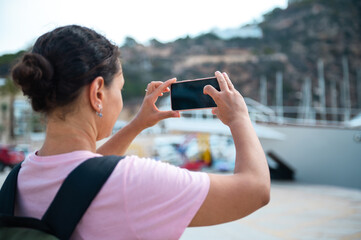 Woman capturing scenic marina view with smartphone camera