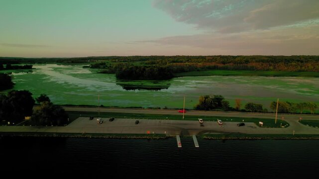 Aerial view of a red car driving near the Green Lake Inlet Boat Launch Site in Ripon, Wisconsin, with a serene water landscape in the background. Peaceful travel along the lakeside.
