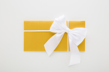 Closed golden wedding envelope with white ribbon on light gray table background. Closeup. Top down view.