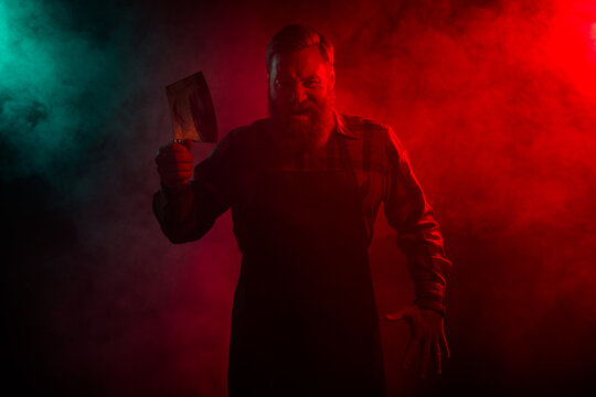 Photo of mysterious serious retired man butcher hold blade knife apron isolated dark red green neon lights background