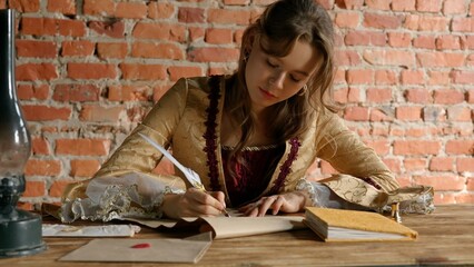 Antique young woman in renaissance dress sitting at table and writing letter with vintage quill pen...