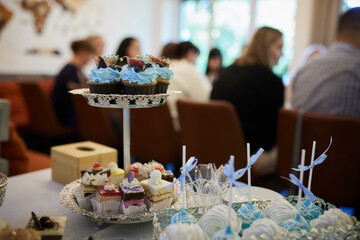 Various pastries and cakes on a beautifully served festive table on the background of a party with people.