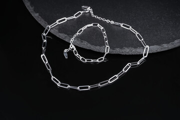 two chains hang from a ceramic dish. metal chain and bracelet on black background close-up....