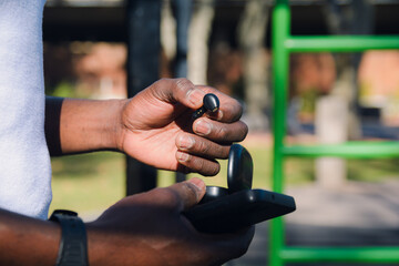 close up black hands of unrecognizable person outdoors holding wireless headset