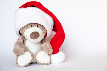 Cute teddy bear toy with smile in huge Santa hat sits on white background where there is copy space.