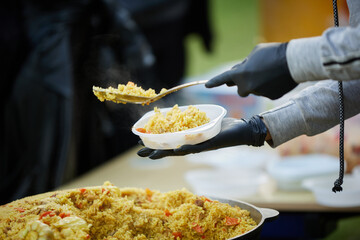 The cook pours pilaf from the cauldron into plastic plates and distributes them to people.