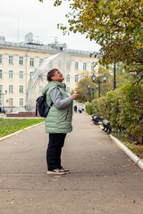 An elderly woman with an umbrella walks in cloudy weather.