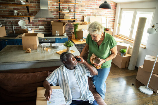 Senior couple unpacking boxes during move into new home with checklist and phone call