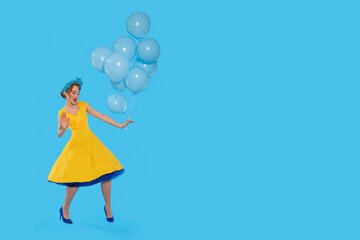 A joyful celebration of color as a woman in a vibrant yellow dress dances with blue balloons against a bright backdrop