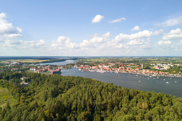 Obraz premium Aerial view of Mikolajki lake town surrounded by lush green forest and clear blue sky, showcasing the serene beauty of nature.
