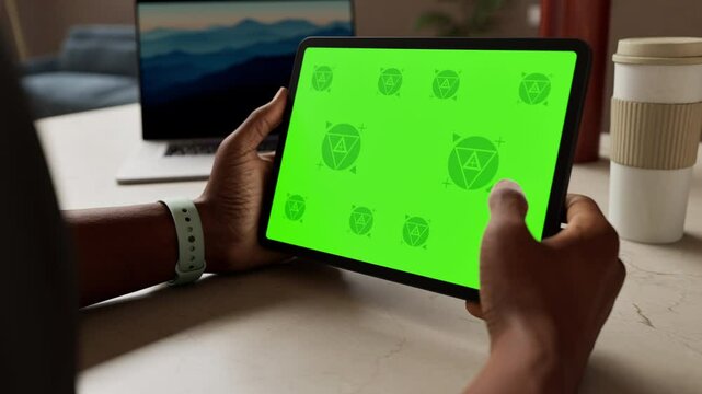 Black African-American man holds a tablet with a green mockup screen in a modern, minimalist office setting