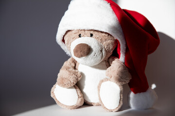 One cute teddy bear toy with smile huge Santa hat sits white background where there is light shadow