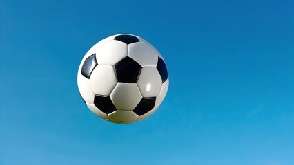 Soccer ball on blue sky, featuring a black and white ball in the air, perfect for sport and football themes