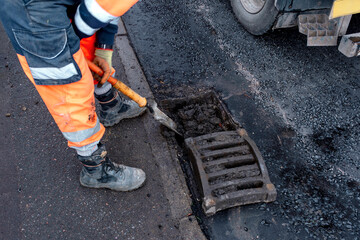 Urban worker clearing debris from storm drain on busy city street during the early morning hours