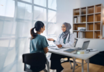 A female doctor in a hijab is talking to a patient in a medical office.