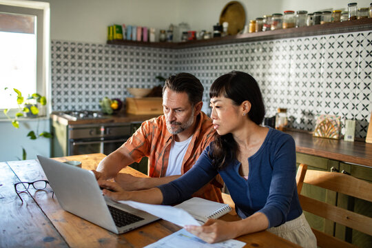 Couple reviewing documents together while using laptop at home