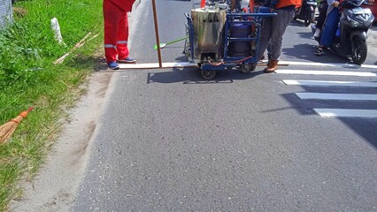 Road workers use hot-melt scribing machines to painting dividing line on asphalt road surface in the city.