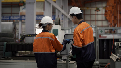 Two workers in orange and blue safety gear are looking at a computer screen. They are likely discussing a project or problem related to their work. Scene is serious and focused