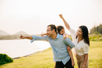Asian family child girl piggyback riding back on father raising hands like flying outdoor nature...