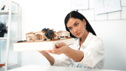 Close up of skilled young beautiful caucasian architect lift house model to check and focus on...