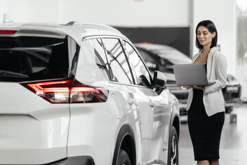 Saleswoman in car showroom selling electric cars. Elegant salesperson, manager working at car...