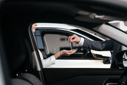 Cropped hands of car dealer giving keys to businesswoman. Car key handover concept. Rent, credit, insurance. Salesman is carrying the car keys delivered to the customer at the showroom.