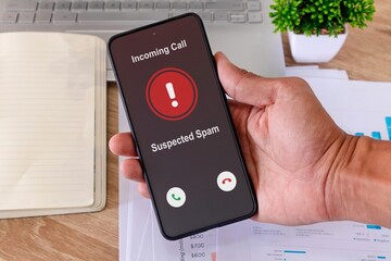 Hand holding a smartphone with incoming call from unknown caller on the screen at workplace....