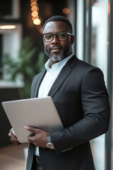 Fototapeta premium Middle-aged Black sales agent in formal attire, holding a laptop with a slight smile, modern technological background.