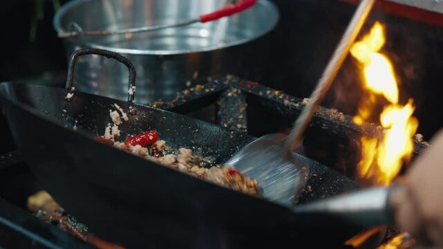 Iron wog pan with ground meat in hand of unknown person over open gas stove with dirty edges. Night market worker preparing spicy nourishment thai chicken salad larb gai with seasonings.