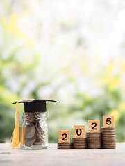 Glass bottle with graduation hat, Wooden blocks with the number 2025 and stack of coins. The...