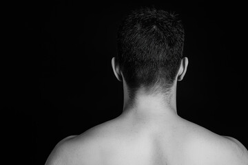 Black and white back view of a shirtless man isolated on dark background