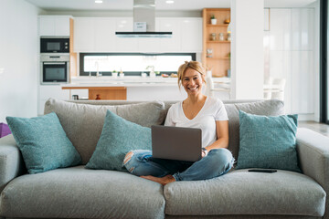 Blonde woman using laptop on sofa