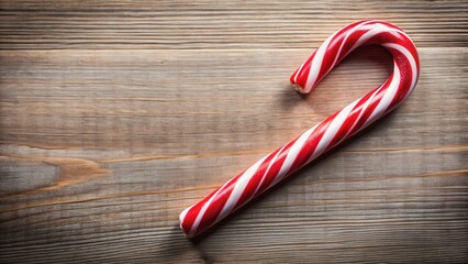 A classic red and white candy cane rests on a wooden surface, its striped pattern creating a festive and inviting scene.