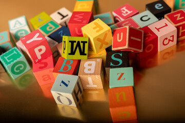 A colorful jumble of alphabet blocks scattered across a golden surface Learning and playing with...