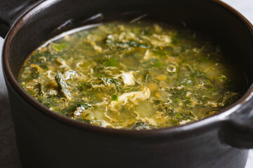 Soup with green sorrel in black ceramic pot on gray background