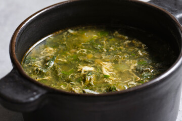Soup with green sorrel in black ceramic pot on gray background