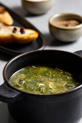 Soup with green sorrel in black ceramic pot on gray background