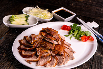 Peking Duck on a white plate served with fresh cucumber, green onions, cilantro and roasted wheaten chinese pancakes on black  wooden background. Chinese food. food concept.