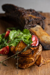 roasted veal rib with baked potatoes and vegetables on a wooden board