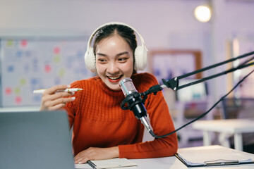 Young asian woman happily records a podcast in her modern home studio, speaking into a microphone...
