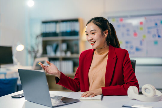 Young asian businesswoman is working late in the office, gesturing while making a video call on her laptop and taking notes