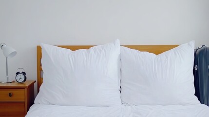 A cozy modern bedroom with white bedding and pillows, complemented by a bedside lamp and a travel suitcase near the headboard, perfect for a restful stay