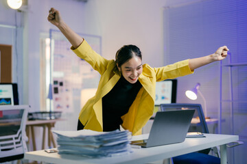 Young professional woman in a modern office celebrates success at work, raising her arms in excitement. The vibrant image reflects dedication and entrepreneurial spirit