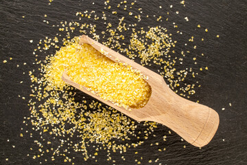 Uncooked corn grits with wooden spoon on slate stone, macro, top view.