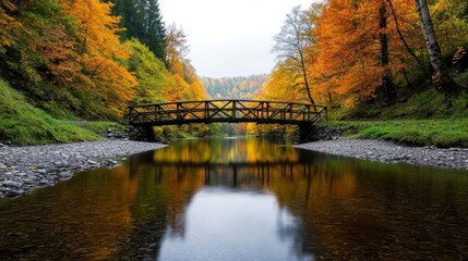 Fototapeta premium Picturesque autumn scene with a wooden bridge over a calm river surrounded by colorful trees.