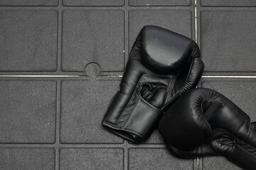 A pair of black boxing gloves rests on a gym's interlocking rubber floor, after a training session. The setting suggests an intense workout, symbolizing the importance of preparation and discipline.