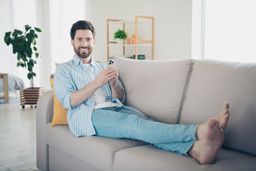 Photo of handsome mature age adult man staying home in living room laying down couch barefoot...