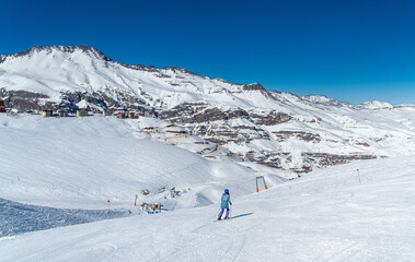 A woman skis down the slopes in the Andes, surrounded by stunning snow-capped mountains. The scene captures the thrill of winter sports.