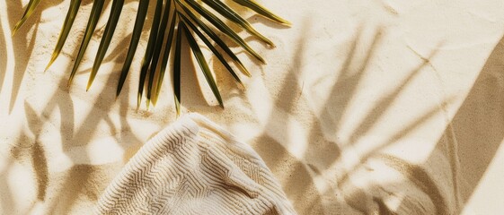 Obraz premium A top-down view of golden sand with a palm leaf casting shadows and a ripple-patterned towel, offering a tropical, beachy vibe.