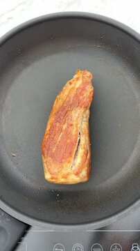 the act of searing a delicious pork tenderloin on a hot cooking pan.
